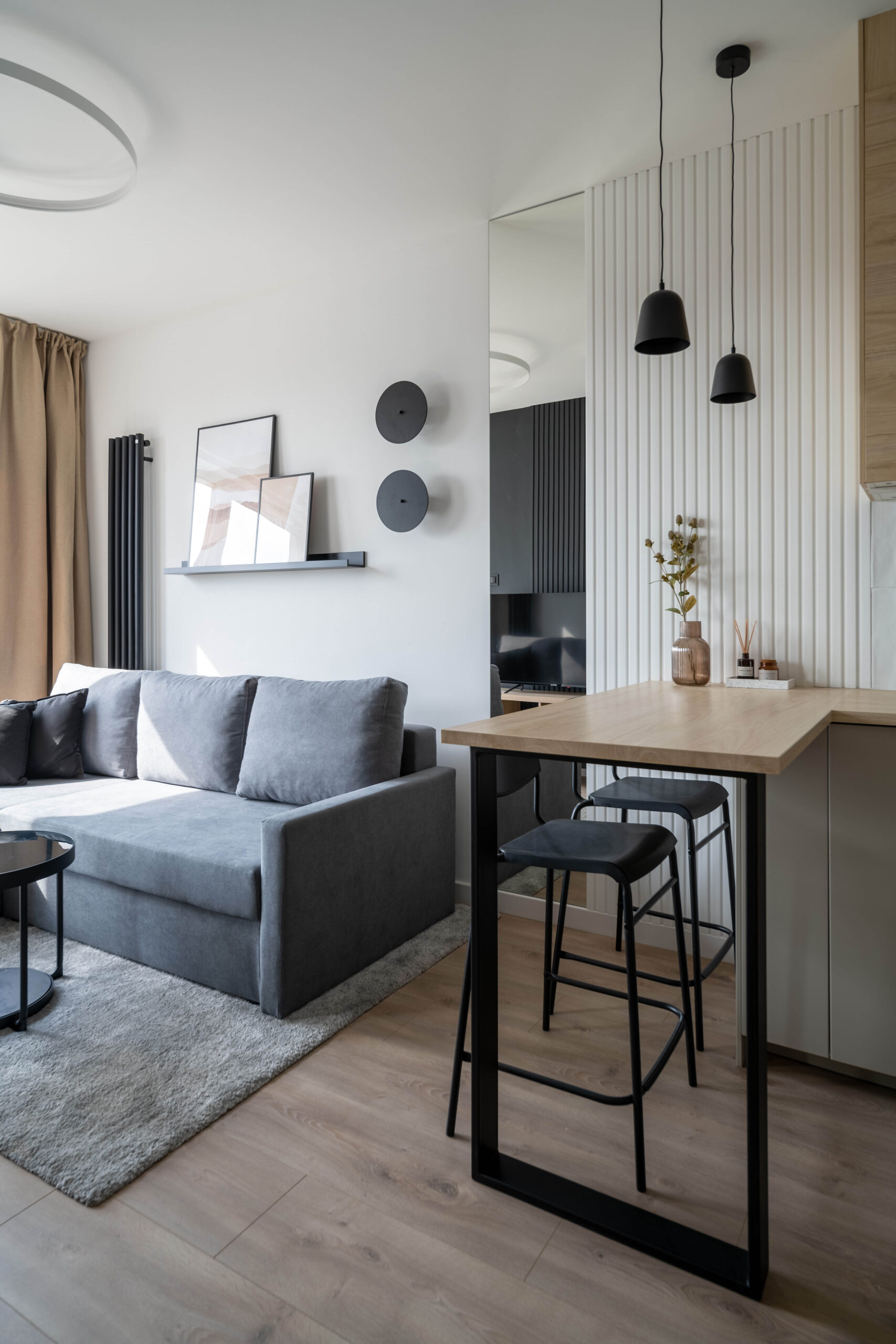 Realizacja KP Project — nowoczesny salon z szarą sofą, barem śniadaniowym i lamelową ścianką oddzielającą strefę dzienną od kuchni